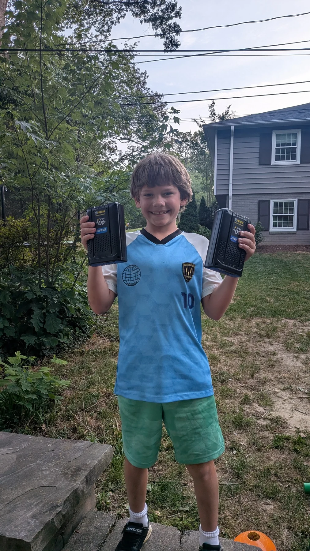 Brady smiling and holding two lawn-tool batteries