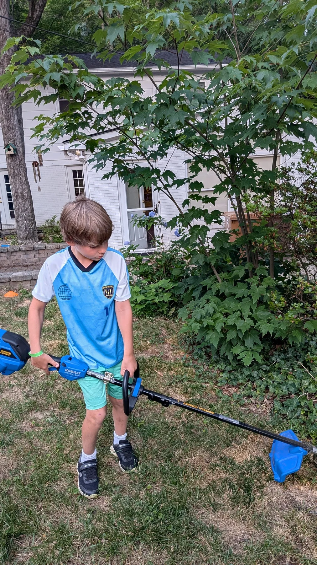 Brady holding a weed trimmer near landscaping